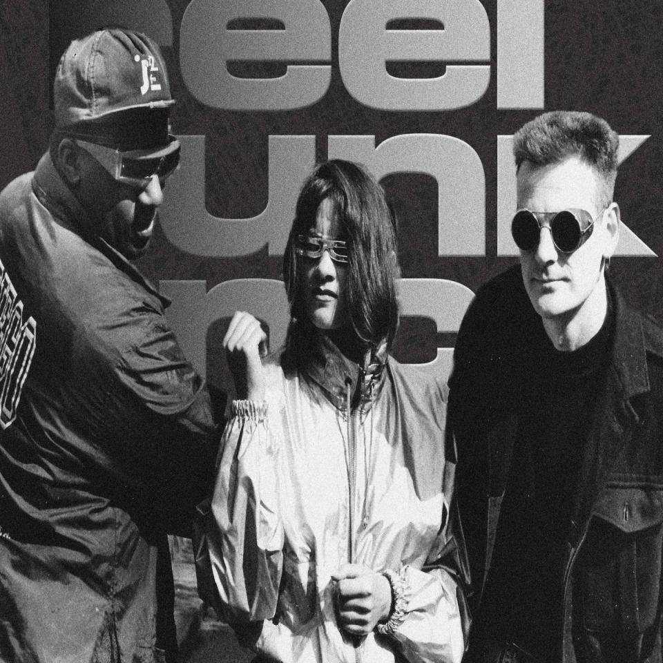 Three piece band standing in front of Reel Funk Inc. logo